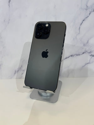 A dark gray Apple iPhone Pro shown from the back, resting on a clear stand against a white marble-patterned background.