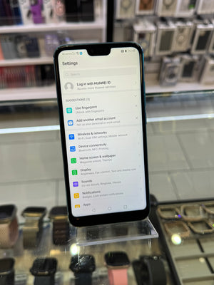 A black smartphone displaying the settings menu, resting on a clear display stand inside a retail store with other watches or devices visible in the blurred background.