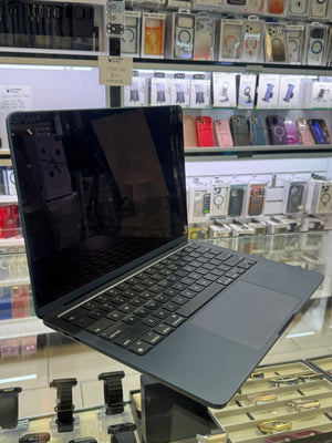 A dark gray laptop with an attached keyboard and trackpad, shown open on a display stand inside a retail store with shelves of phone accessories in the background.
