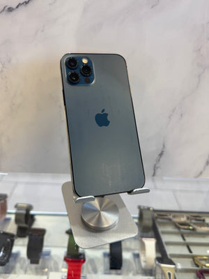 A dark blue-gray iPhone Pro shown from the back, resting on a silver magnetic display stand on a white marble surface.