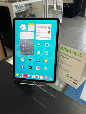 Tablet displaying a home screen with various app icons on a stand, with a 'Afterpay it.' flyer in the background.