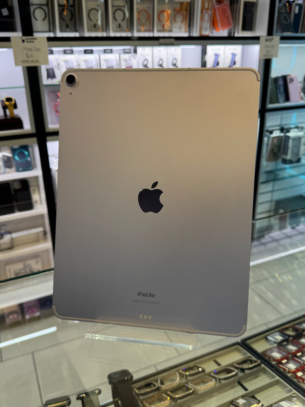 An Apple iPad Air in silver displayed on a clear stand inside a retail store, showing the back of the device with the Apple logo and 'iPad Air' text.