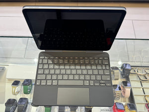 A dark gray wireless keyboard and trackpad combo attached to a tablet with a black screen, displayed on a glass retail counter with smartwatches in the background.