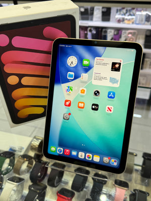 An Apple iPad with a black front bezel and colorful screen displaying various apps, shown in a retail store setting with its original box in the background.