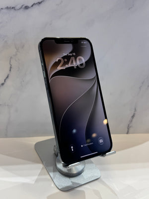 A black iPhone displayed vertically on a silver metal stand, set against a light gray marble-patterned background.