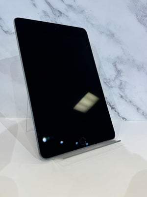 A black tablet with a silver edge, displayed standing upright on a clear acrylic stand against a white marble-patterned background.