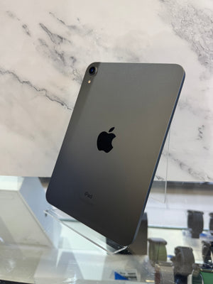 A dark gray Apple iPad Pro shown from the back, standing on a clear display stand against a white marble-patterned background.