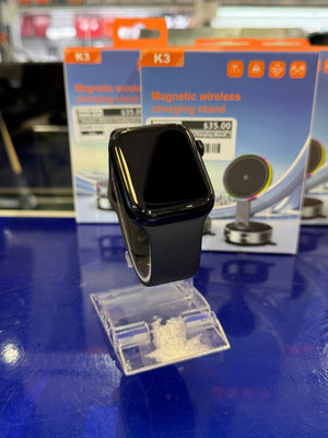 Black smartwatch on a blue display stand with a magnetic wireless charging stand in the background