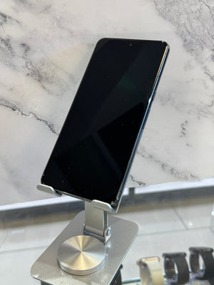 A black smartphone displayed at an angle on a metallic silver stand, set against a white and gray marble-patterned background.