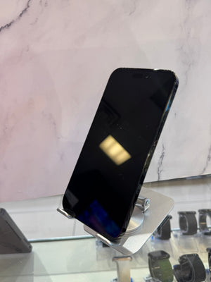 A black smartphone displayed upright on a silver stand inside a retail setting, with a marble-patterned wall in the background and other accessories partially visible on a glass counter.