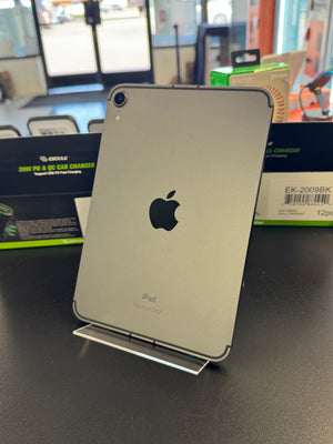 An Apple iPad with a silver metallic back and black camera lens, resting on a small white stand on a dark gray surface.