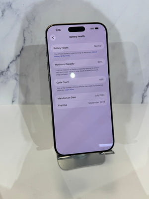 A black smartphone displayed upright on a small metal stand against a light marble-patterned background. The phone screen shows the iOS Battery Health settings page.