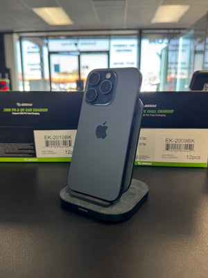 A dark gray Apple iPhone Pro stands upright on a charging dock on a black tabletop, with Geekse charging box packaging visible in the blurred background.
