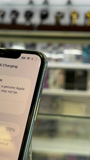 A close-up of a smartphone showing a charging status screen, with blurred Apple product displays in the background.