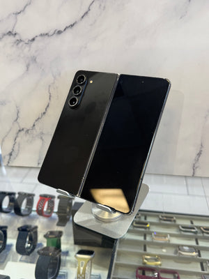 A black Samsung Galaxy S21 Ultra foldable smartphone displayed open on a metallic stand, with a marble-patterned wall and watch display case in the background.