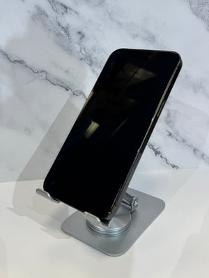 A black smartphone displayed upright on a silver metal stand against a white marble-patterned background.