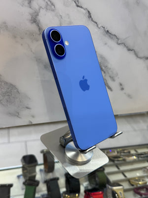 A blue Apple iPhone with a dual-camera system, displayed on a silver stand against a white marble-patterned wall.