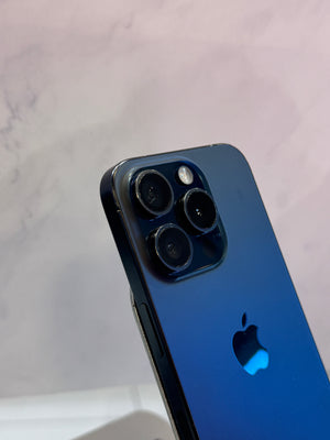 Close-up of the back of a blue Apple iPhone showing the triple-camera system and Apple logo, photographed against a light marble-patterned background.