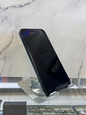 A black smartphone with a glossy screen, resting on a silver metal display stand. The background features a white marble-patterned wall and a glass display counter.