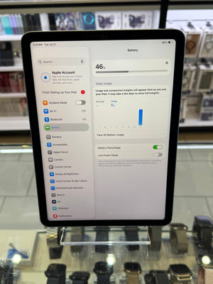 An Apple iPad displaying the battery settings screen, standing on a clear display stand inside a retail store.