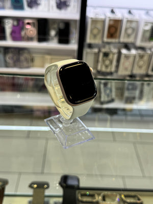 A smartwatch with a cream-colored band and a gold-toned bezel, displayed on a clear stand inside a retail store.