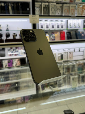 A dark green Apple iPhone 12 Pro shown from the back, resting on a clear acrylic display stand inside a retail store.