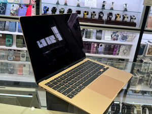 Gold laptop on a glass table with a store display of watches in the background