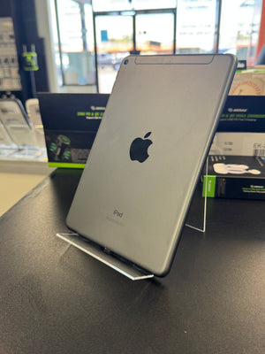 A silver Apple iPad shown from the back, resting on a clear acrylic display stand on a dark tabletop inside a retail store.