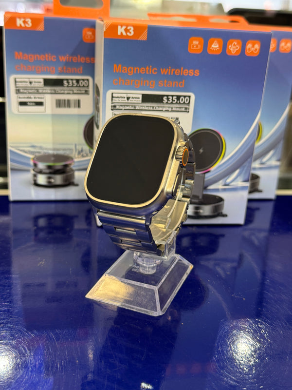 Apple smartwatch with a metal link band on a stand and a magnetic wireless charging stand in the background