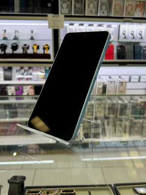 A light blue smartphone with a black screen, displayed on a clear acrylic stand inside a retail store.