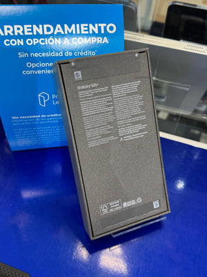 Samsung Galaxy S10+ replacement battery standing upright on a clear display stand, with its back panel showing specifications and logos. A blue Samsung promotional box is visible in the background on a blue tabletop.
