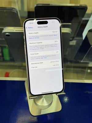 A smartphone displayed upright on a stand in a retail setting, showing the Battery Health settings screen on the home screen. The phone has a black front with a silver-toned metallic stand and base.