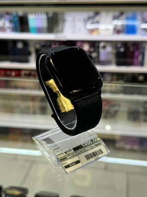 Black smartwatch with a black band on a stand in a store setting. 