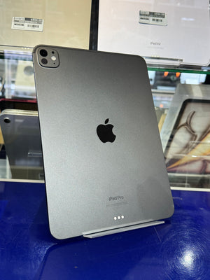 A dark gray Apple iPad Pro standing upright on a display stand in a retail or showroom setting, with the Apple logo visible on the back.