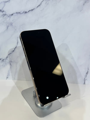 A black smartphone with a silver metallic edge stands upright on a small silver display stand against a white marble-patterned background.