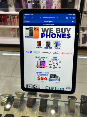 A tablet device displaying a promotional webpage for buying and selling phones, photographed inside a retail display case with watch cases visible in the background.