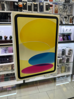 An Apple iPad box standing upright on a glass display counter in a retail store. The front of the box features a colorful abstract design with yellow, blue, and pink shapes inside a black border.