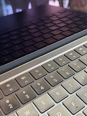 A close-up of a silver and black wireless keyboard in the foreground, with the reflection showing on the black screen.
