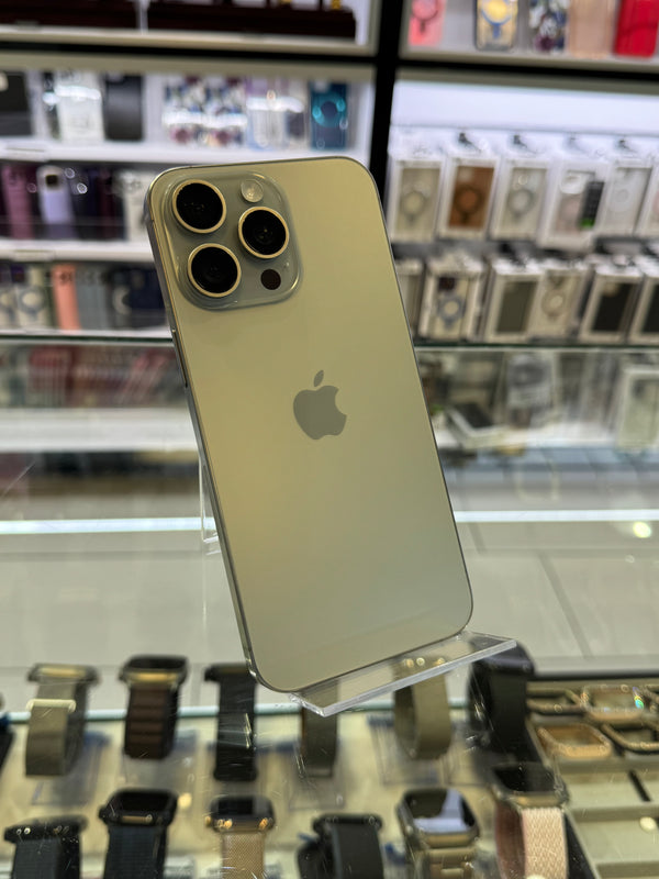 An Apple iPhone 13 Pro displayed on a clear stand inside a retail store, with its triple-lens camera system and the Apple logo clearly visible against a blurred background of shelves and watches.