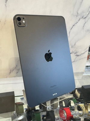 A dark gray Apple iPad Pro shown from the back, standing upright on a display stand in front of a marble-patterned wall.