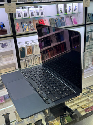 A dark laptop with a matching keyboard and trackpad, shown open on a glass display stand inside a retail store.