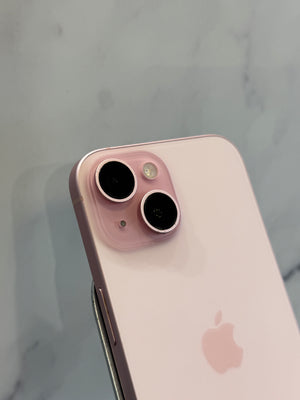 A close-up of the back of a light pink Apple iPhone showing the dual camera lenses and the Apple logo, set against a light gray marble background.