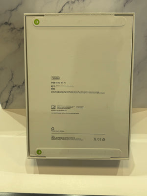 The back of an Apple iPad box showing product specifications and regulatory text, photographed on a white surface with a marble-patterned background.