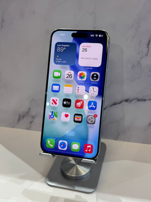 A black Apple iPhone with a large display showing the home screen, resting on a silver metal display stand against a light gray marble-patterned background.