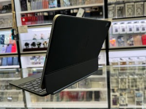 A black tablet in a protective folio case with an attached keyboard, shown at an angle inside what appears to be a retail store with display cases in the blurred background.