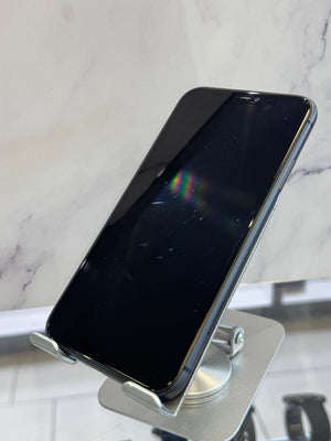 A black smartphone with a screen protector resting on a silver metal stand, set against a white marble-patterned background.