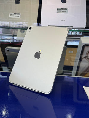 A silver Apple iPad Pro shown from the back, standing on a glossy dark blue display counter inside a retail store. The Apple logo is clearly visible in the center.