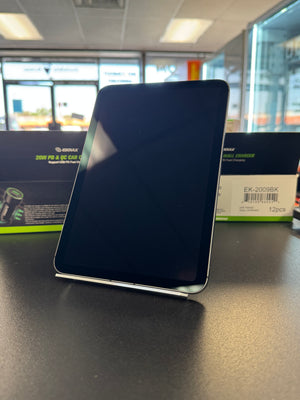 A black rectangular electronic device, likely a power bank or charger, standing upright on a dark surface with its retail box visible in the blurred background.