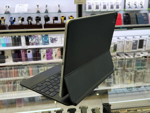A black tablet in a folio-style keyboard case, shown standing open on a glass display counter inside a retail store. The background shows shelves of other electronic accessories and cases.