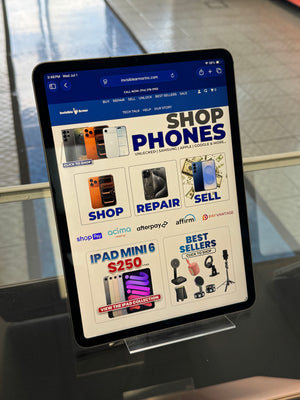 A tablet device mounted on a display stand, showing a website page with phone and iPad Mini promotional content.